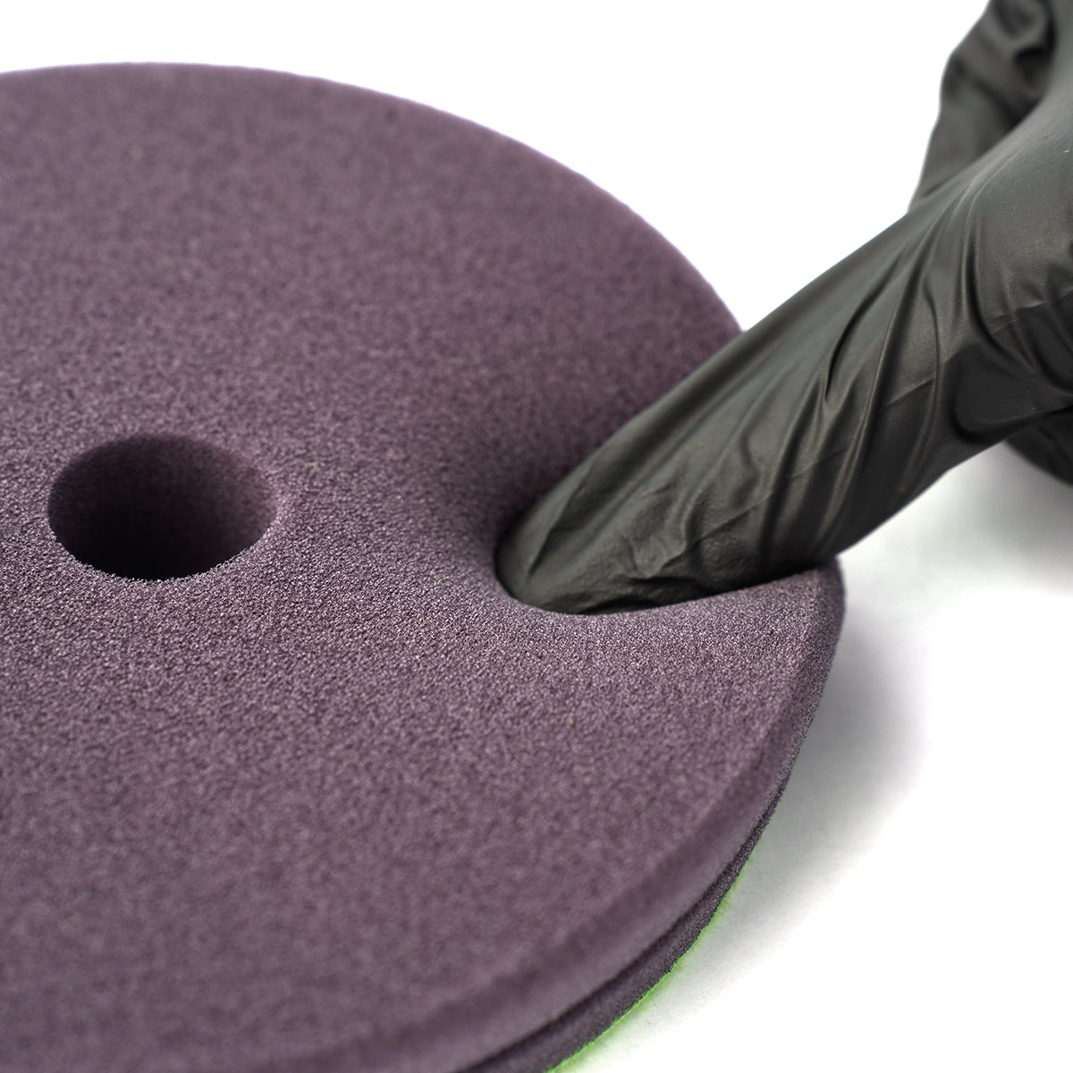 Purple sanding disc with a hole, held by a black-gloved hand on a white background