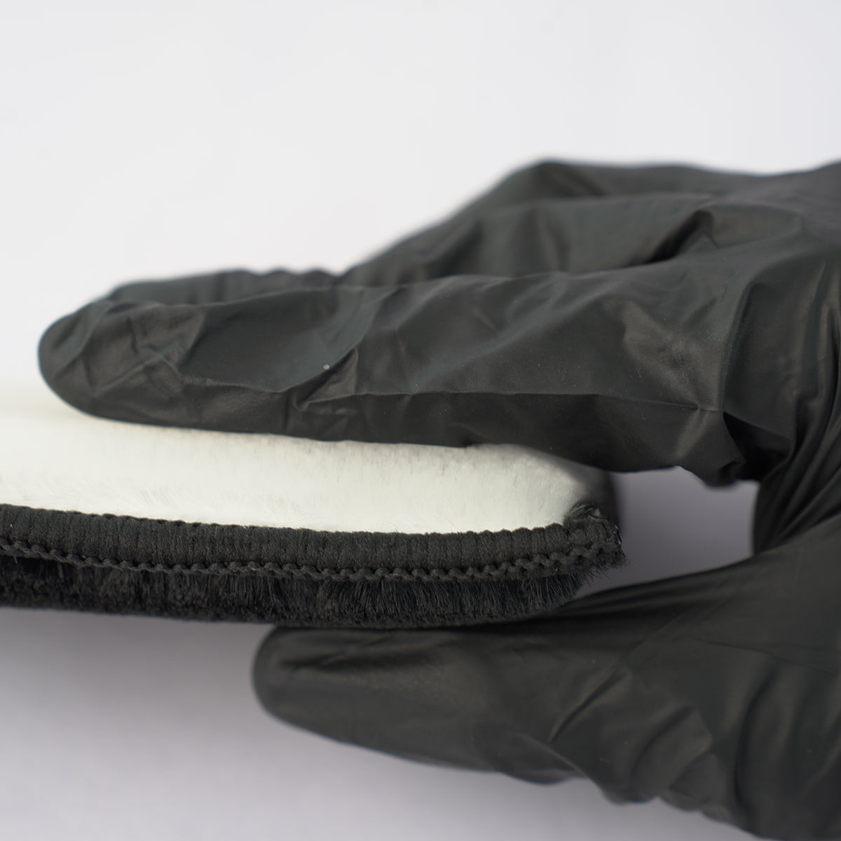 Black glove holding a white foam block on a white background