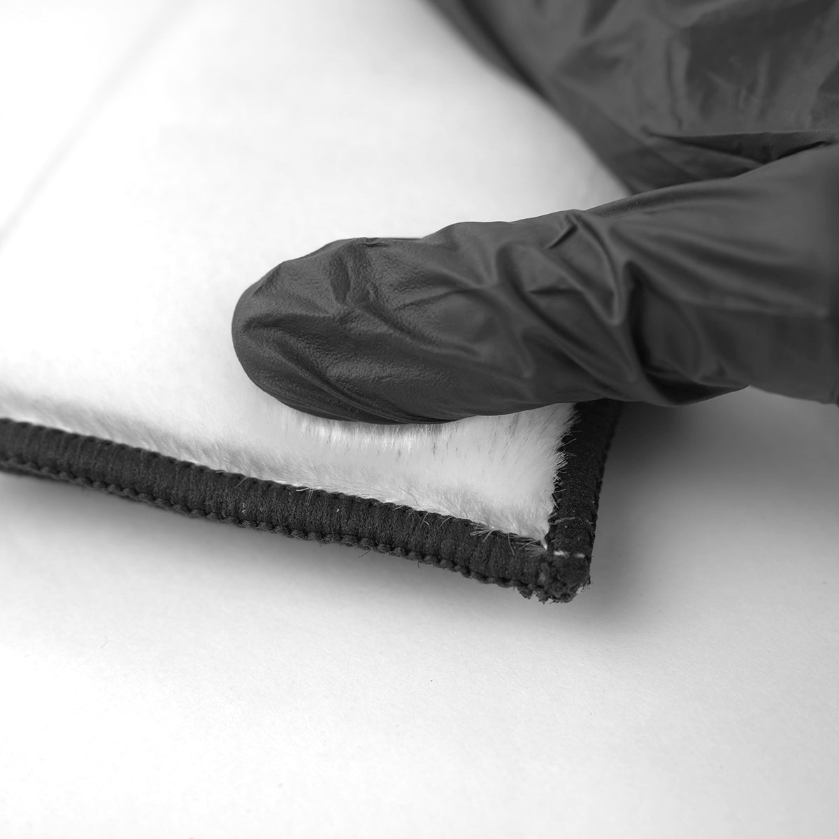 Black glove touching a folded piece of black and white fabric on a white background