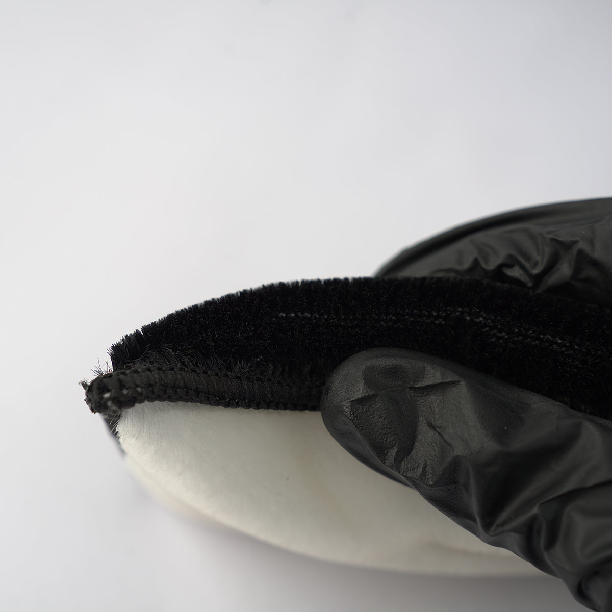 Black glove holding a white object with a black textured handle against a white background
