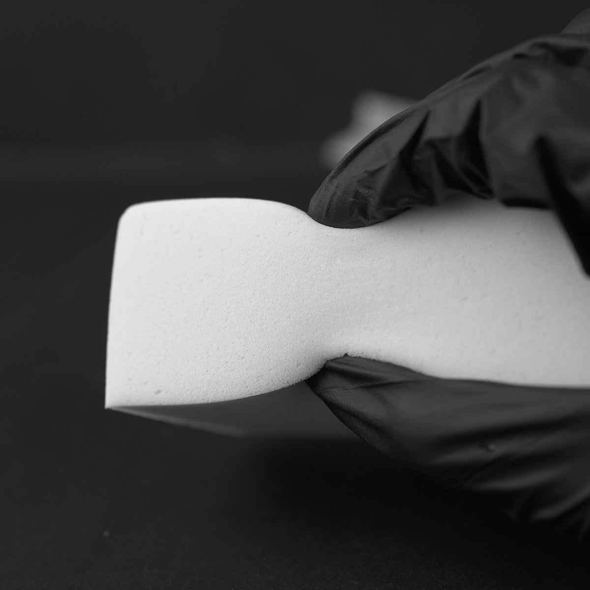 White foam block held by a gloved hand against a black background