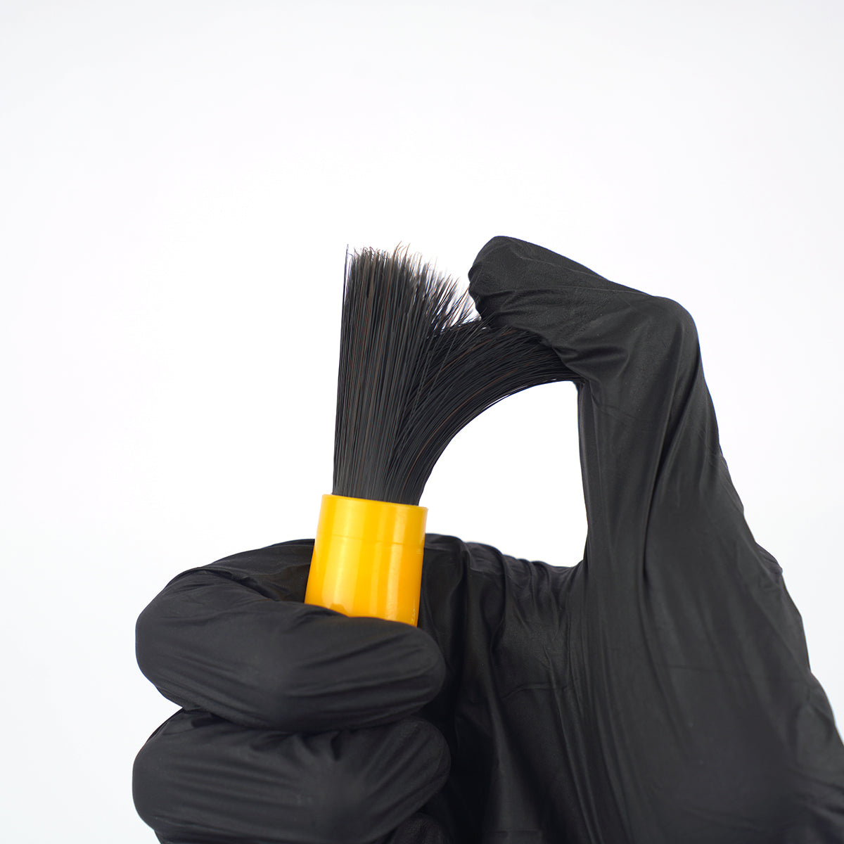 Black glove holding a black brush with a yellow handle against a white background