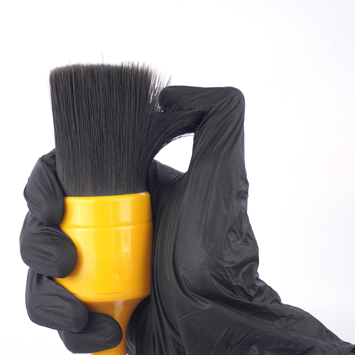 Yellow brush with black bristles held by a gloved hand on a white  Bbackground