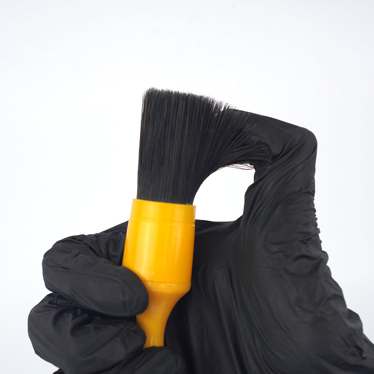 Black glove holding a yellow brush against a white background