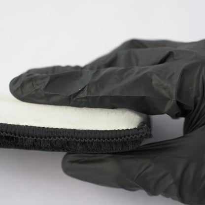 Black glove holding a white foam block on a white background