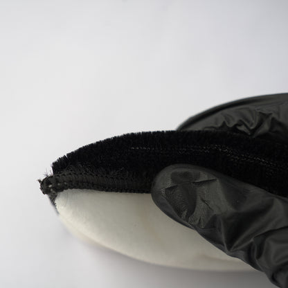 Black glove holding a white object with a black textured handle against a white background