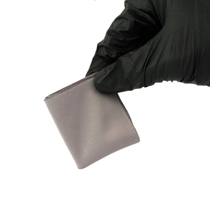 Hand wearing a black glove holding a metallic square object on a white background