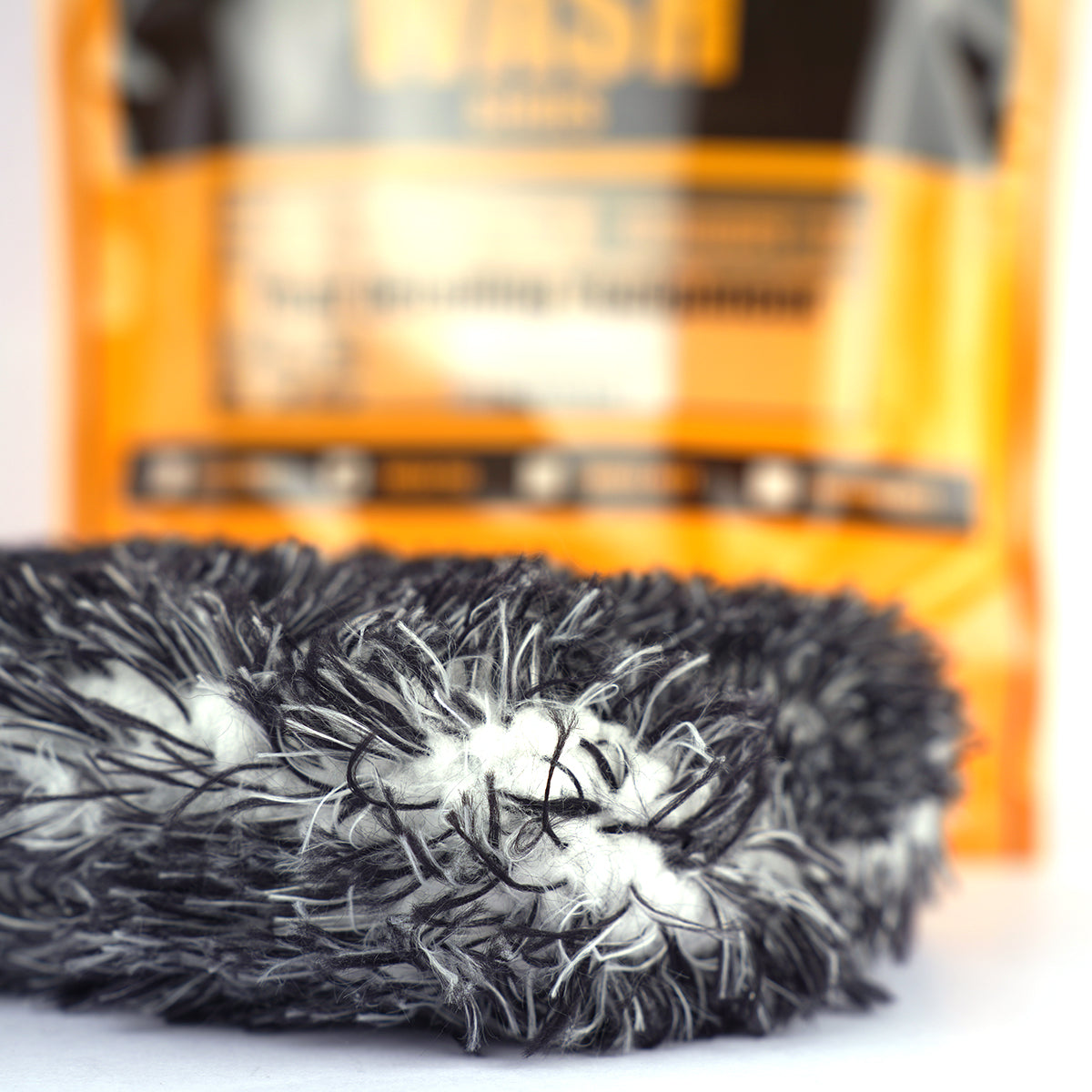 Close-up of a black and white scrubber with a blurred orange and black package in the background.